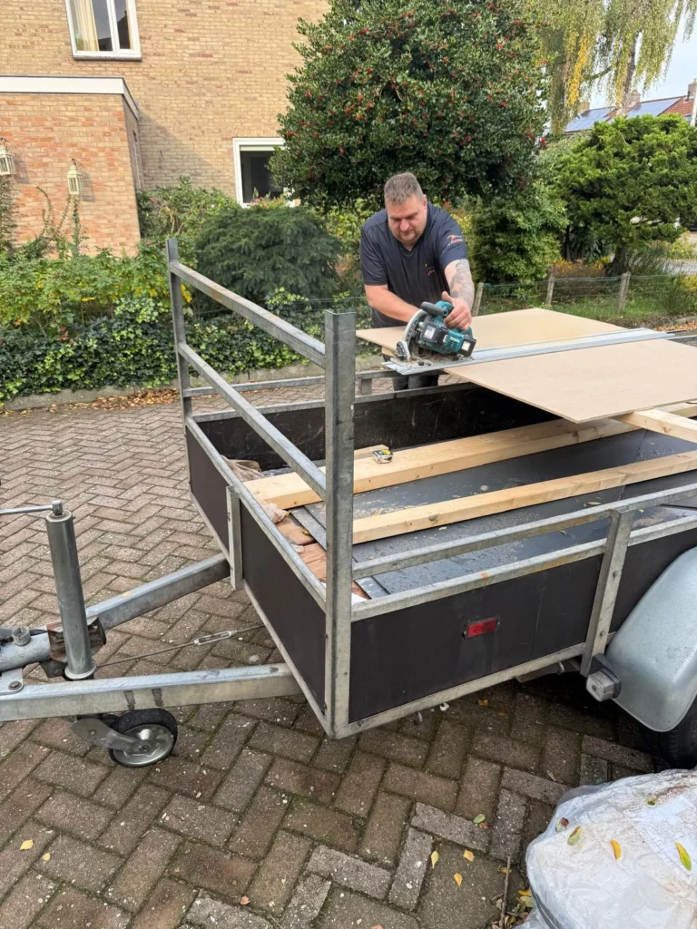 Vakman met cirkelzaag zaagt plaatmateriaal op een aanhanger in Apeldoorn