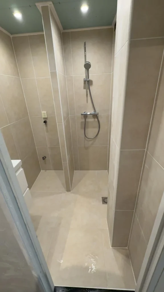 Nieuw betegelde douche met beige wandtegels, glijstang en vloerputje in Apeldoorn