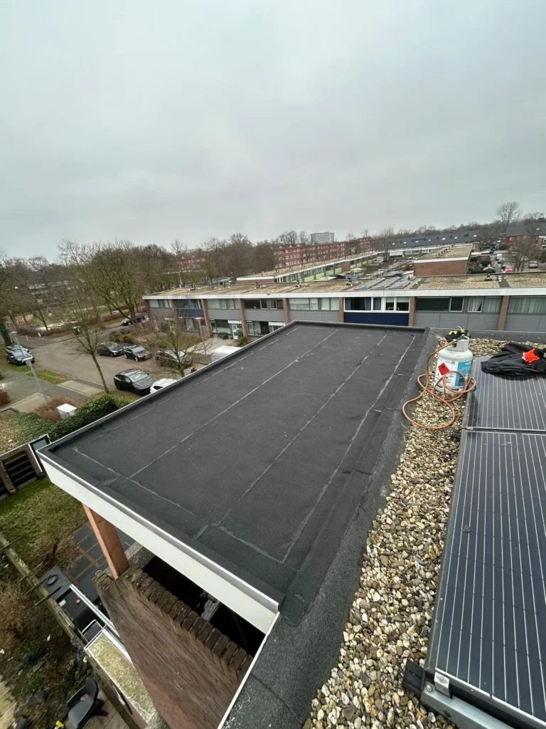 Plat dak met nieuwe bitumen dakbedekking naast zonnepanelen en grind in Apeldoorn