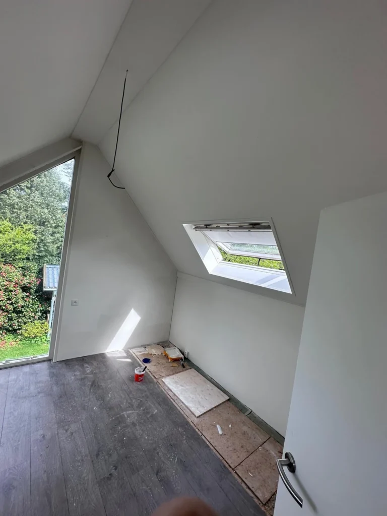 Zolderkamer met wit afgewerkte schuine wanden, dakraam en laminaatvloer in Beekbergen