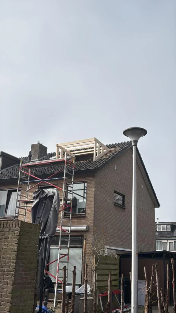 Houten frame van een nieuwe dakkapel op een pannendak met steiger tegen de gevel in Klarenbeek