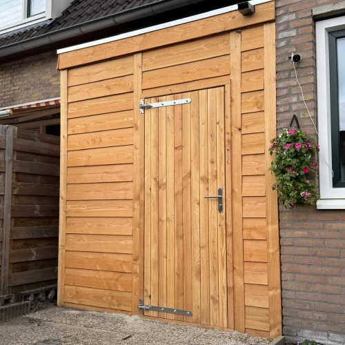 Houten berging van lariks met deur tegen de gevel van een rijwoning in Apeldoorn