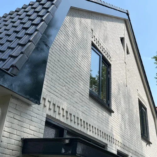 Wit geschilderde gevel met donker pannendak en zwart boeiboord in Apeldoorn
